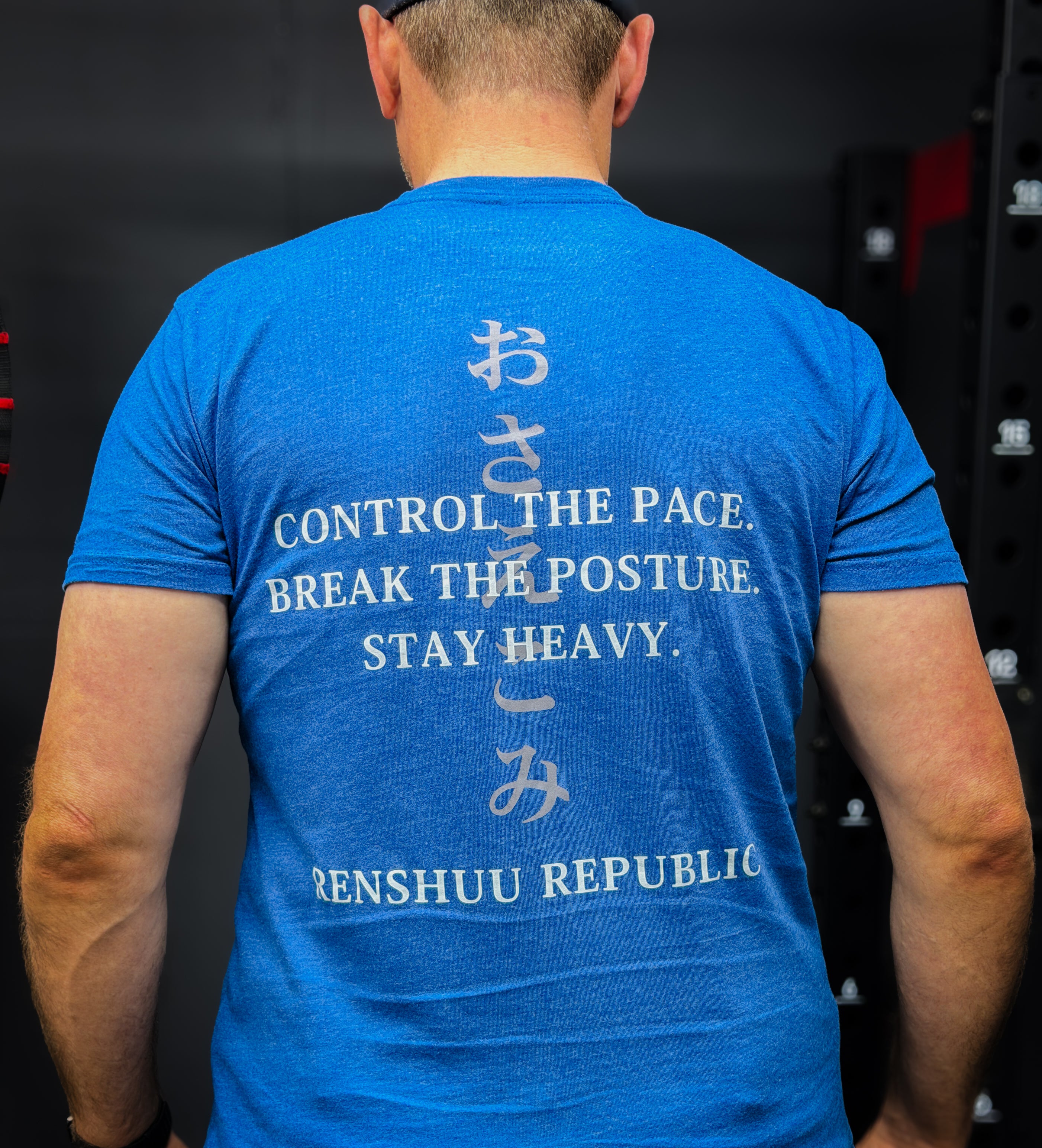 Person wearing a blue t-shirt with text and symbols on the back, standing against a dark background.