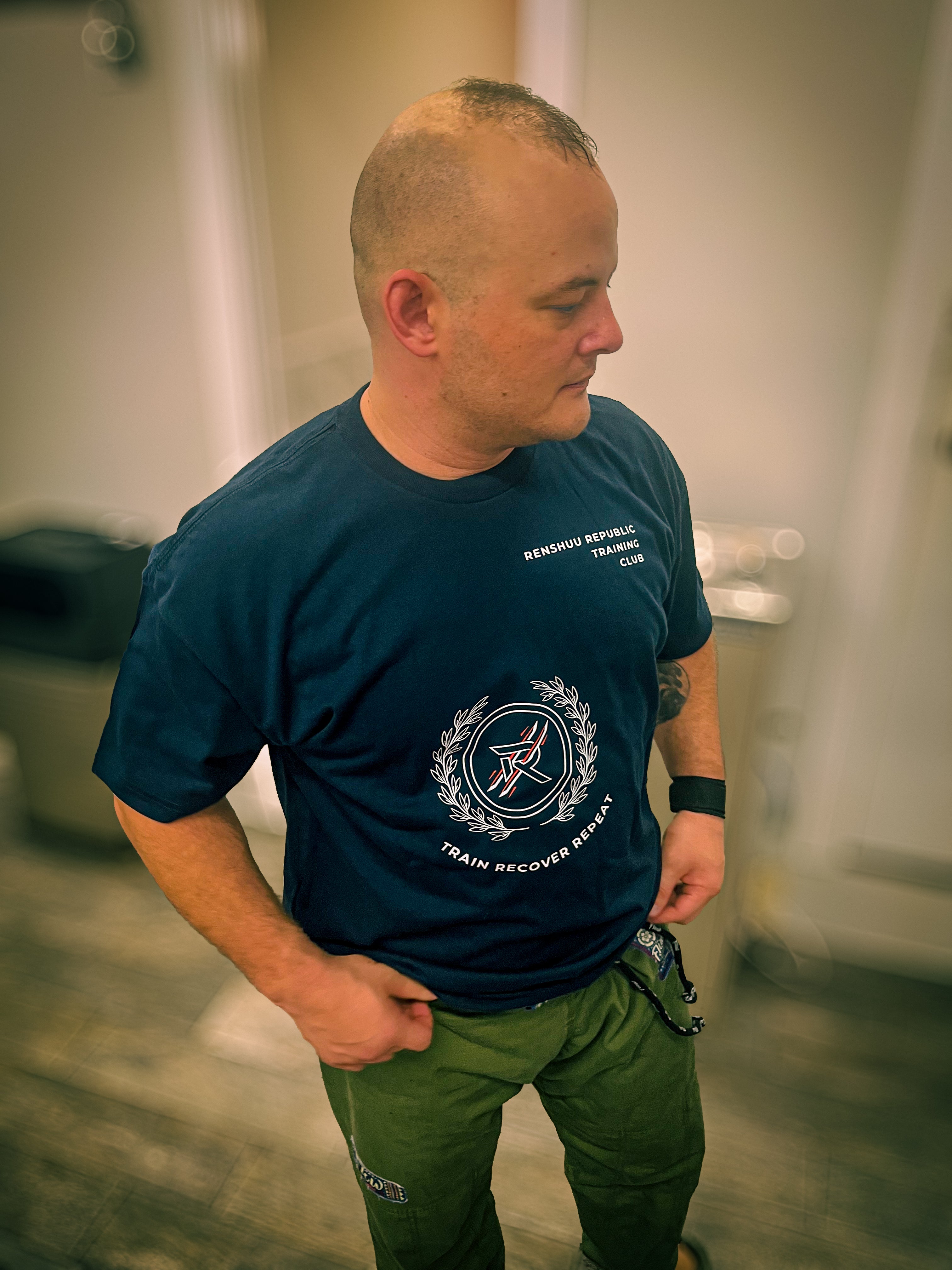 Man wearing a blue t-shirt with a logo and text, standing in a room.