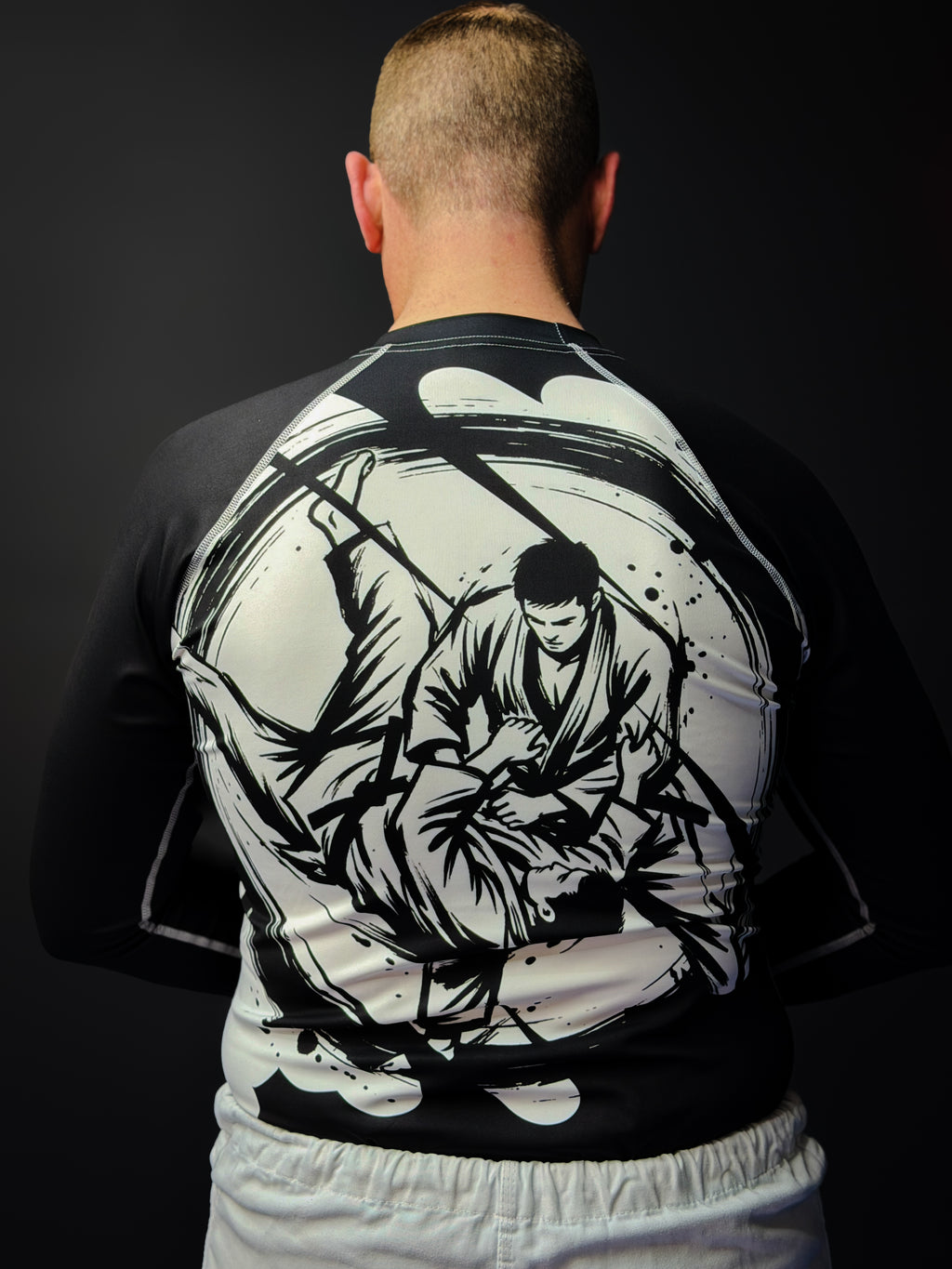 Person wearing a black long-sleeve shirt with a white martial arts design on the back against a dark background.
