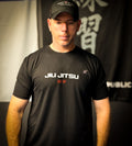 Man wearing a black 'JIU JITSU' t-shirt in front of a dark background with text.
