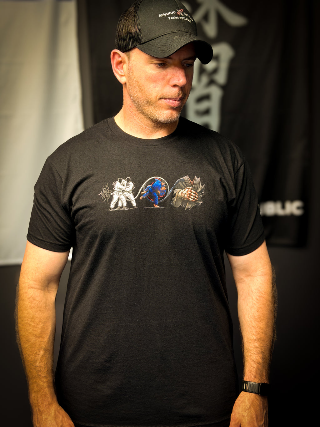 Man wearing a black t-shirt with graphic designs and a black cap indoors.