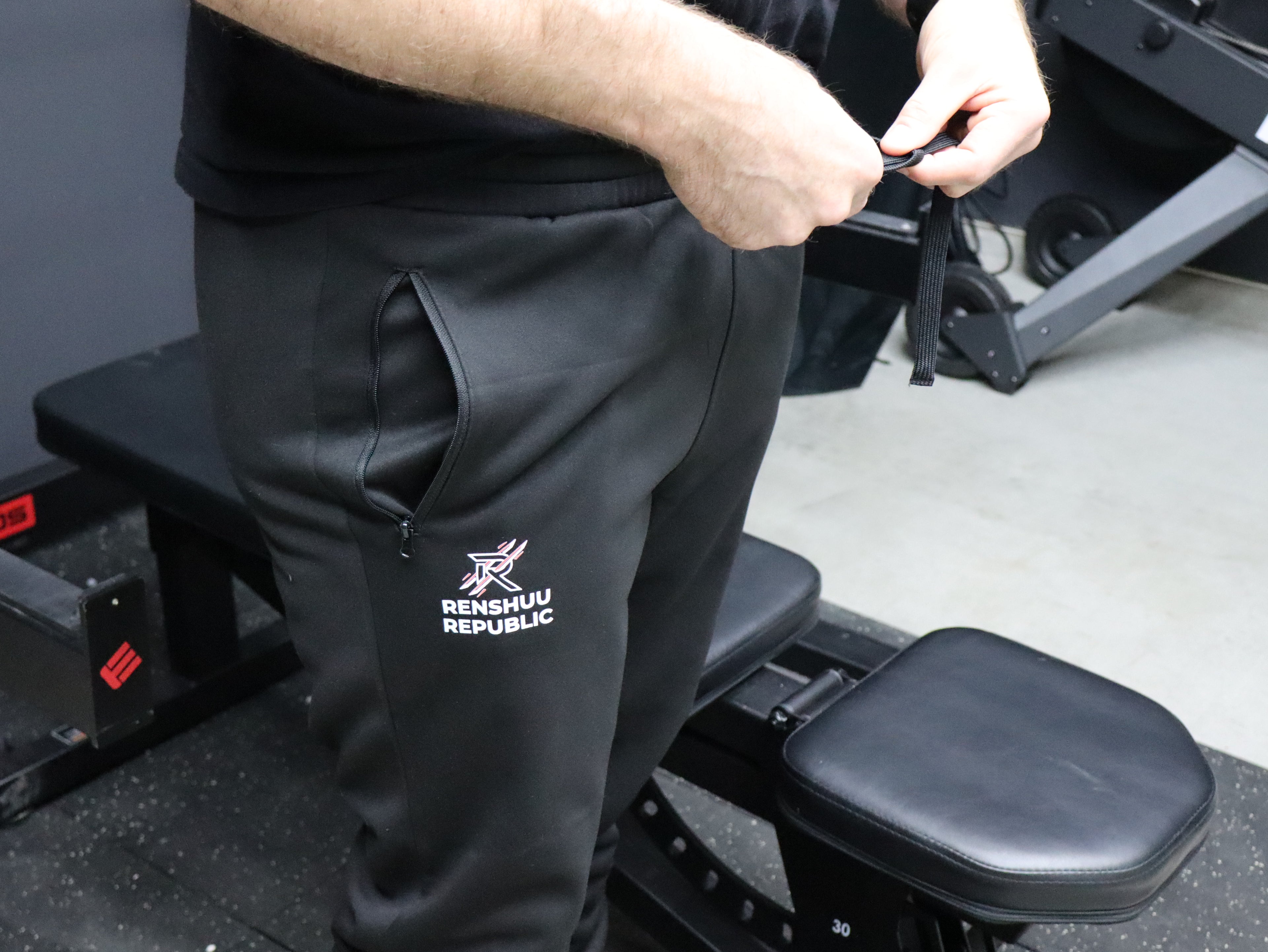 Person wearing black pants with a visible brand logo in a gym setting