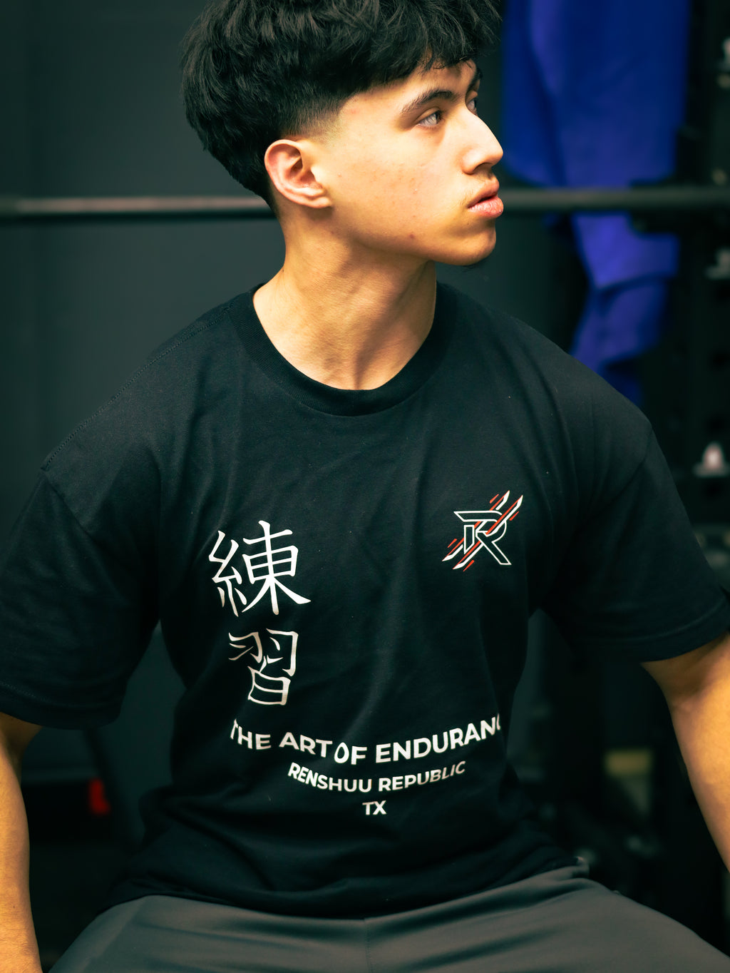 Person wearing a black t-shirt with text and graphics, sitting indoors.