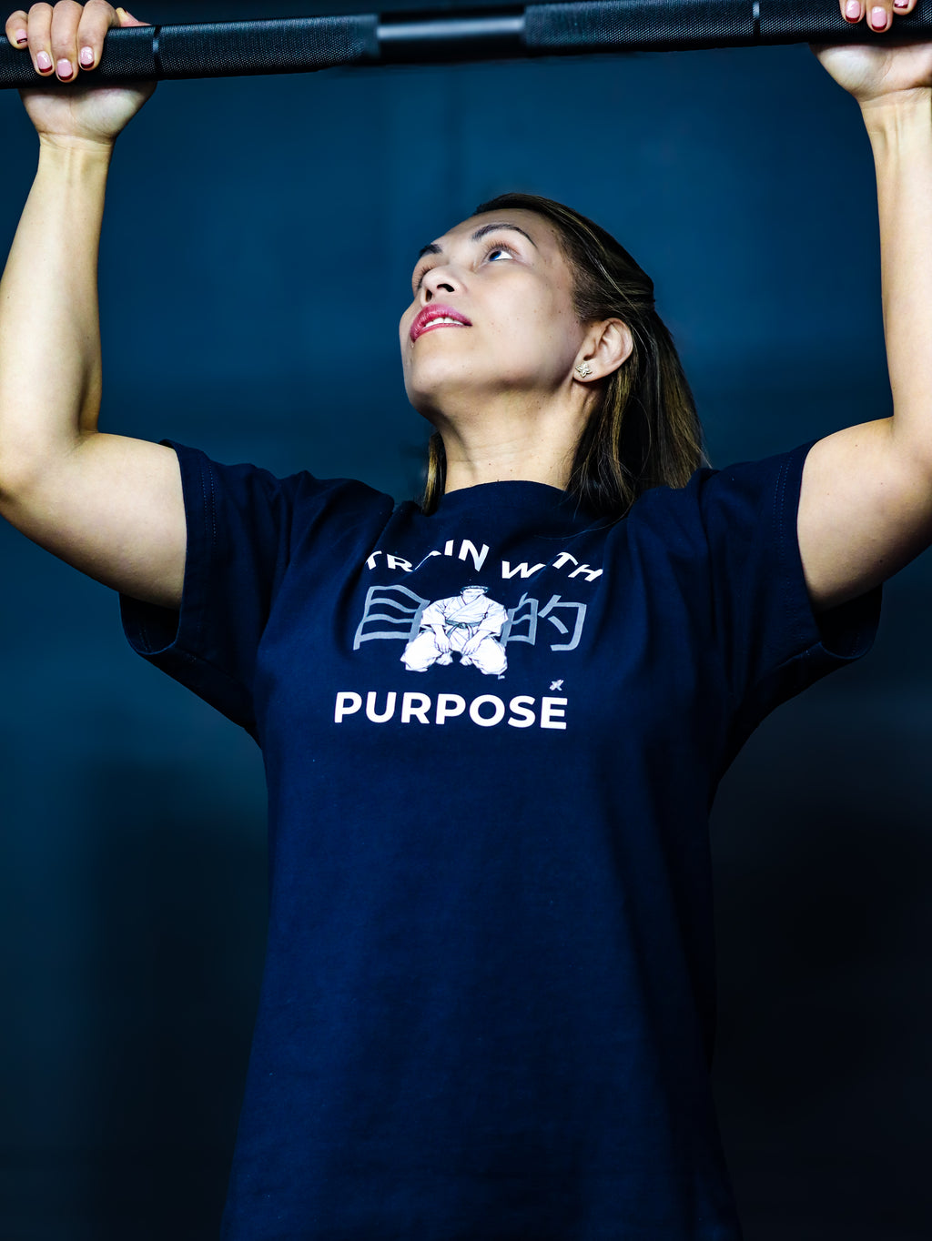 Person wearing a navy blue t-shirt with 'Purpose' text and graphic, lifting weights against a dark background