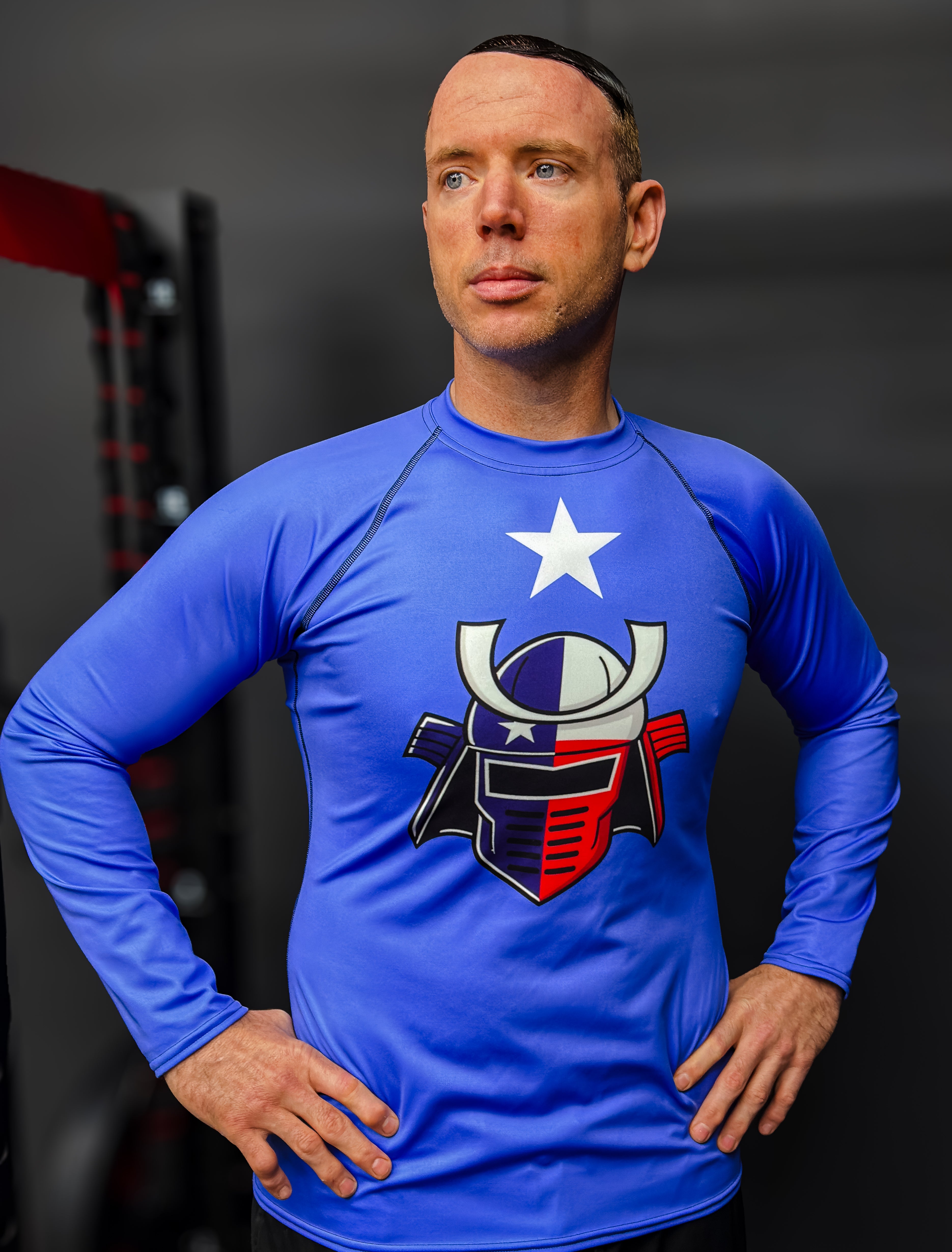 Man wearing a blue athletic shirt with a logo, standing against a dark background.