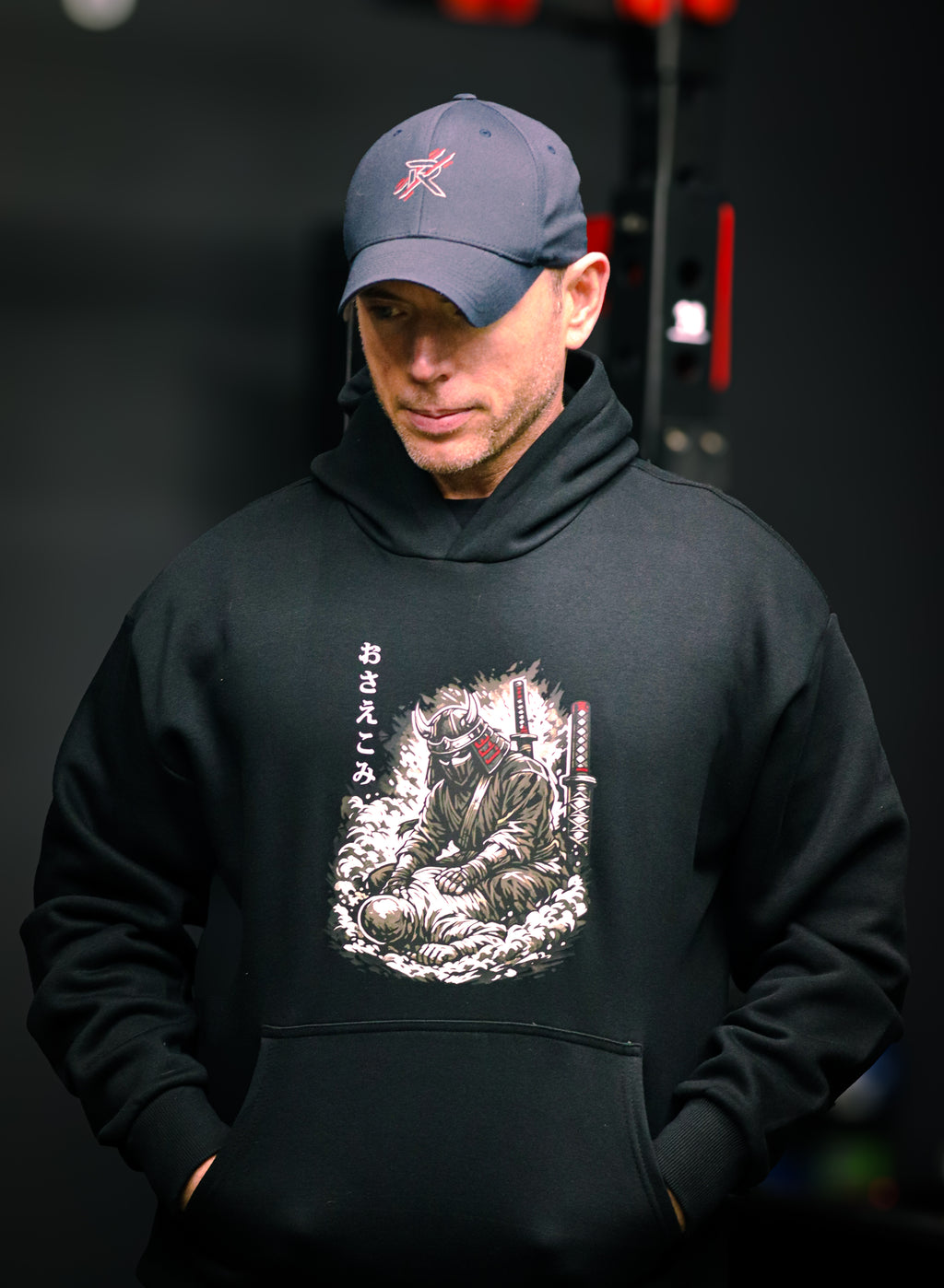 Person wearing a black hoodie with a graphic design and a cap in a dark setting